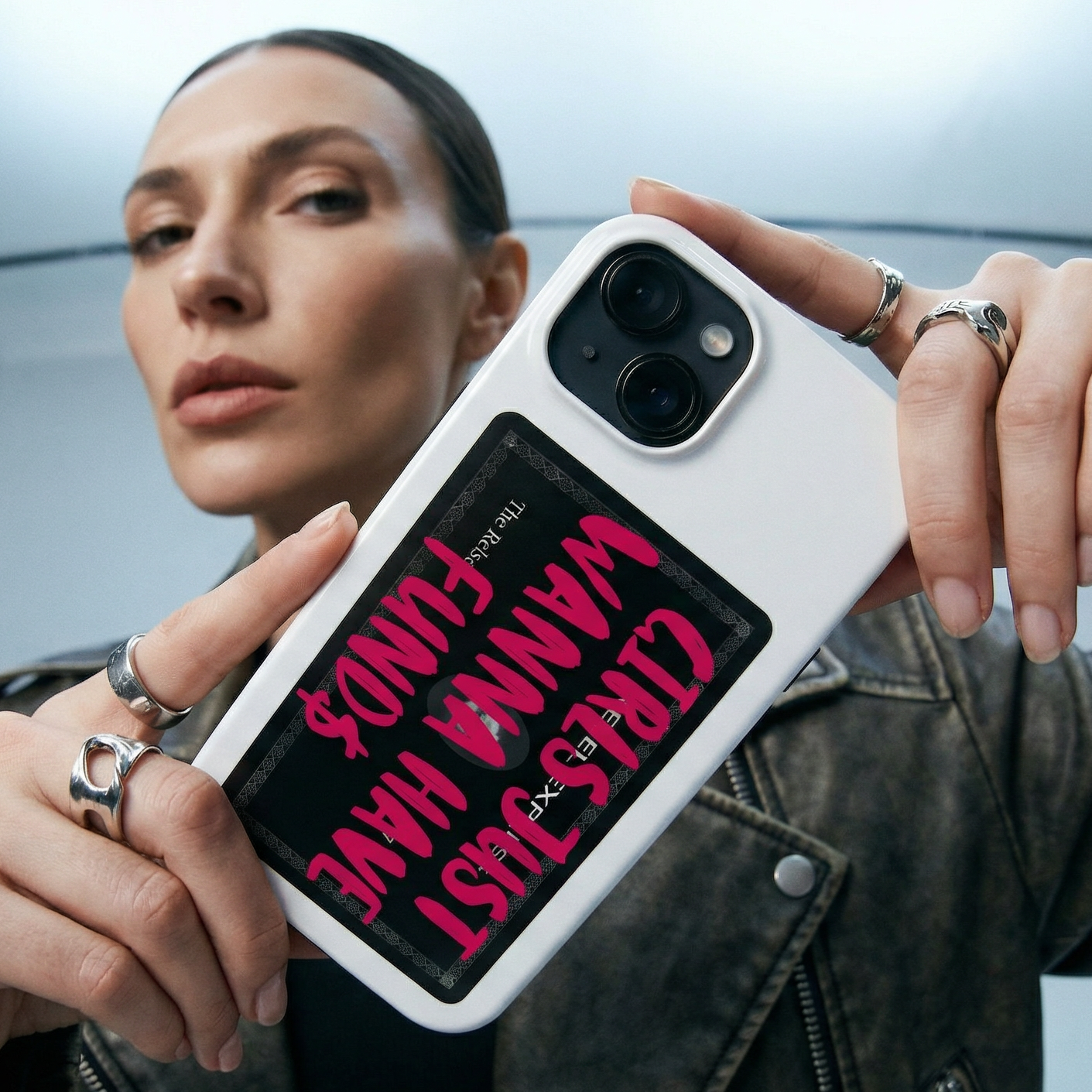 Person holding a phone case with text design, wearing a leather jacket indoors.